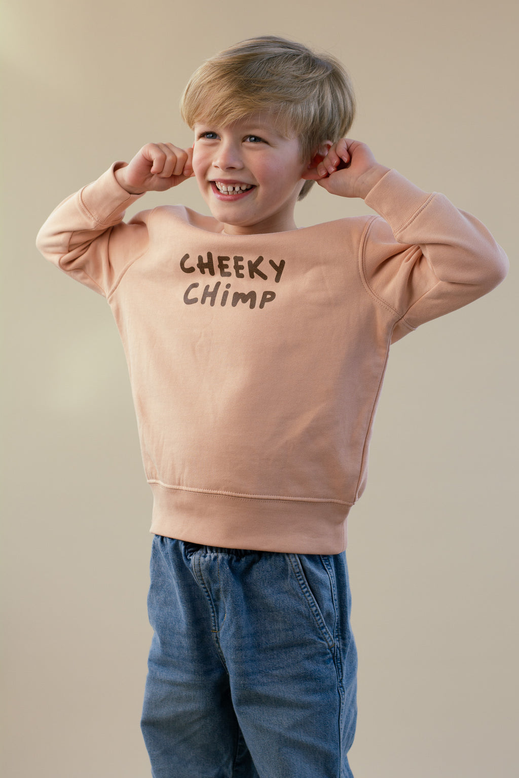 Child wearing a peach sweatshirt with 'Cheeky Chimp' text on a beige background