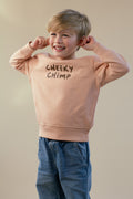 Child wearing a peach sweatshirt with 'Cheeky Chimp' text on a beige background