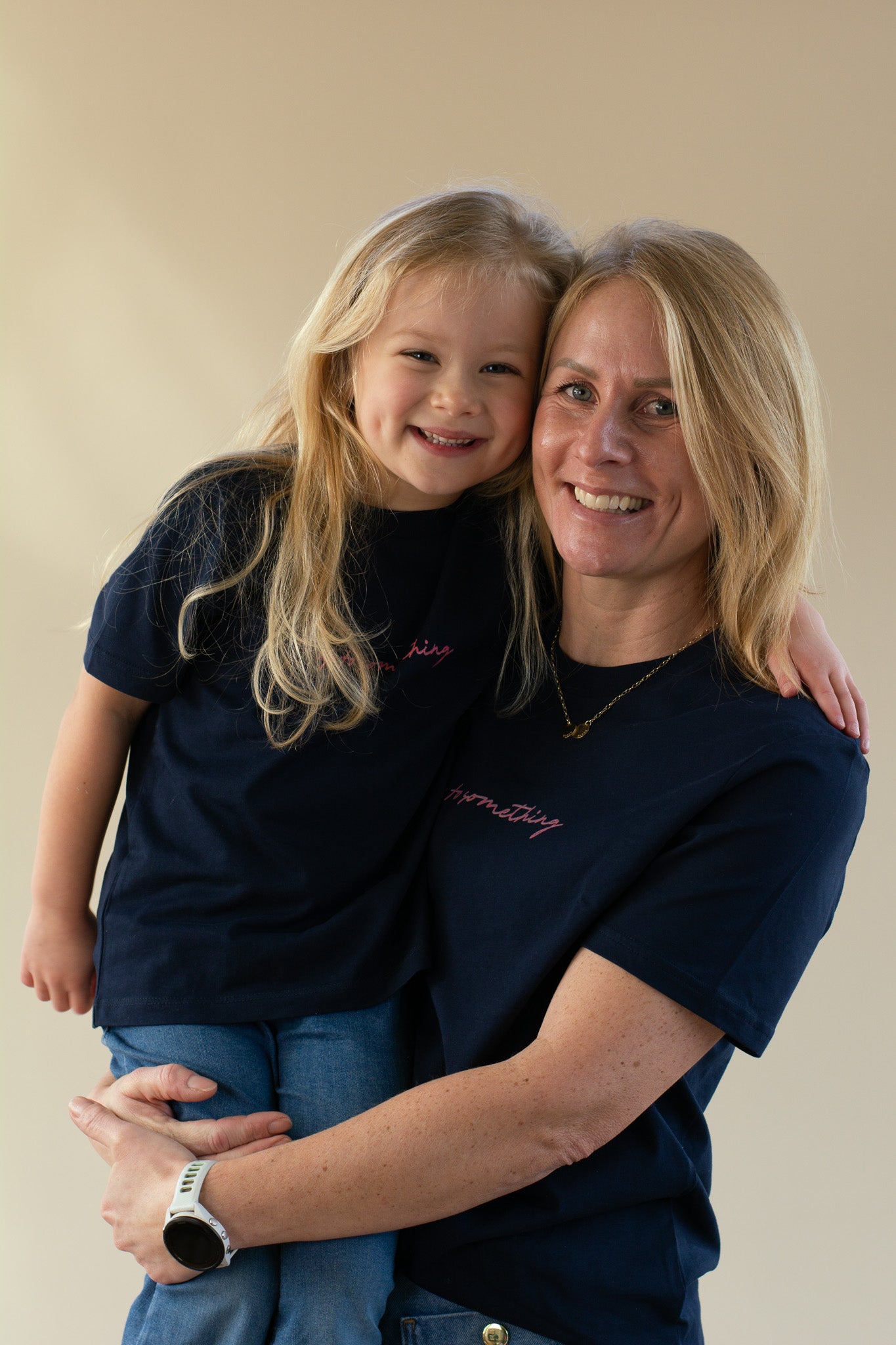 Woman and young girl wearing matching navy blue shirts against a beige background