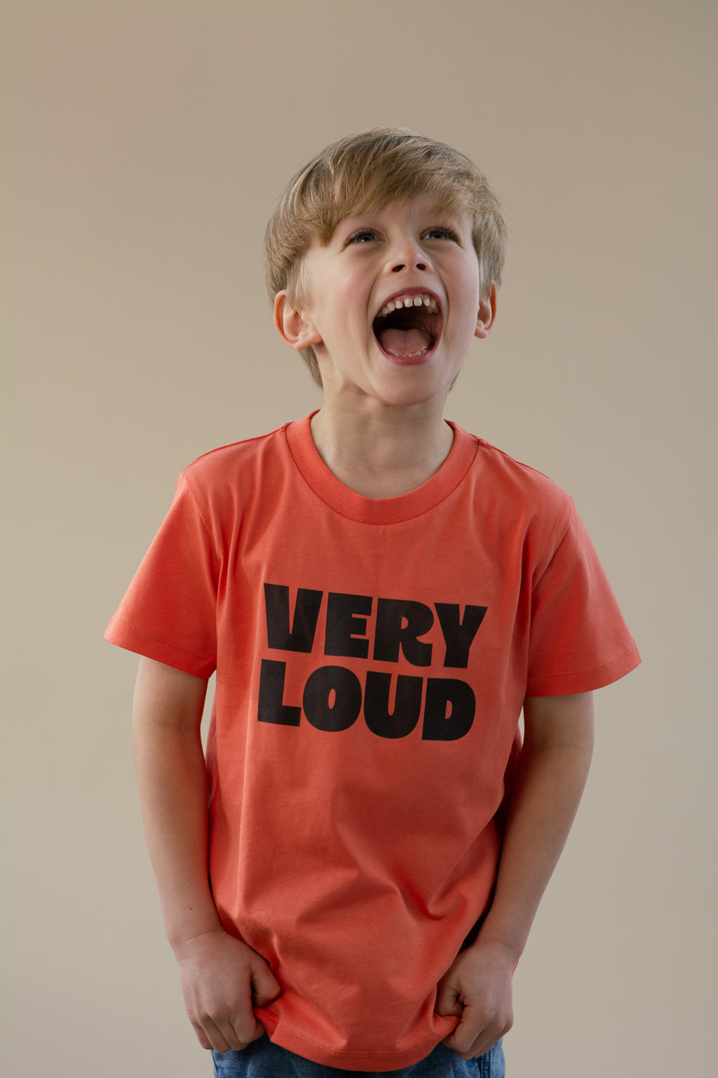 Child wearing an orange 'VERY LOUD' t-shirt against a beige background
