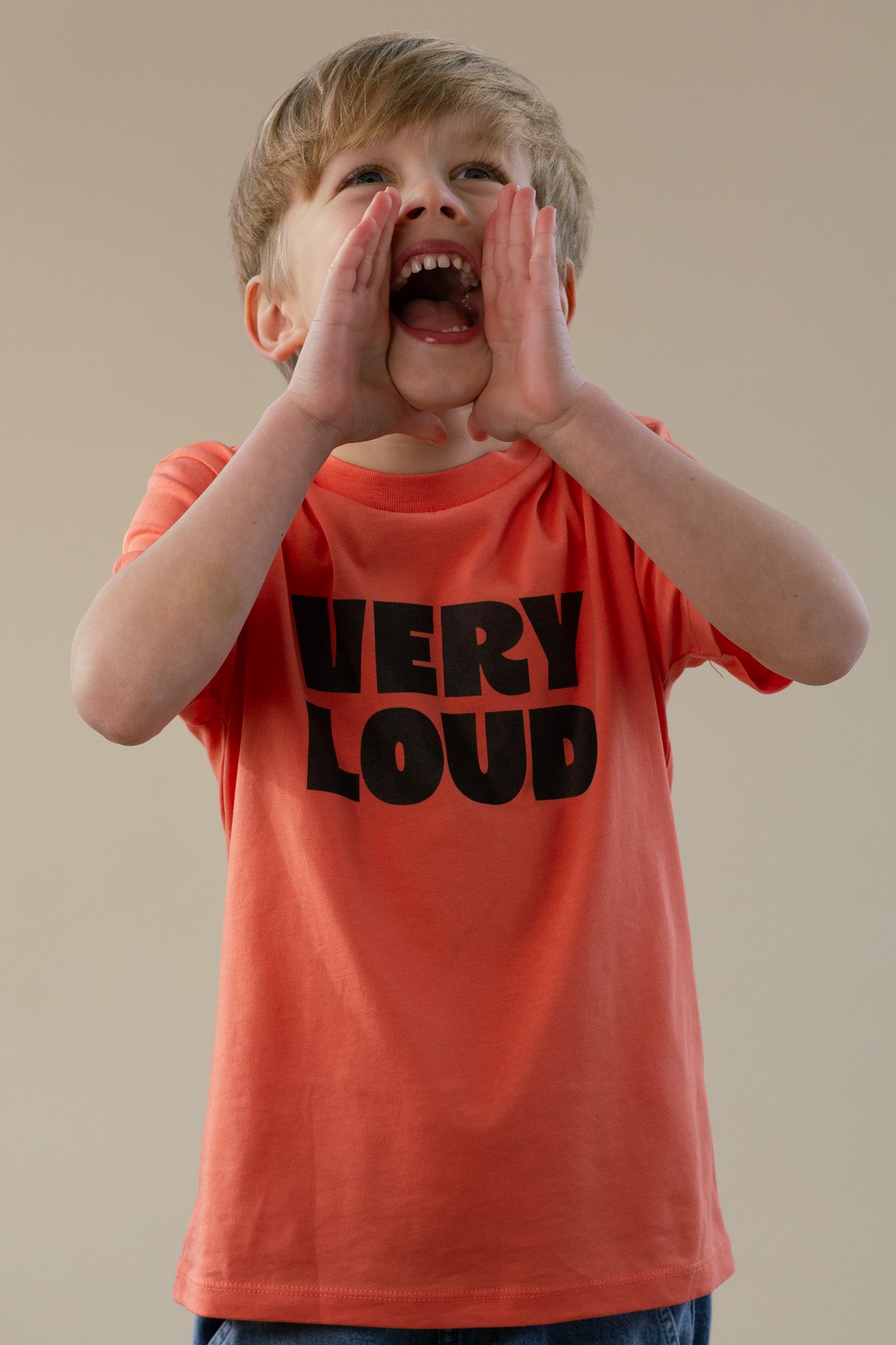 Child wearing a 'VERY LOUD' t-shirt, shouting with hands over mouth