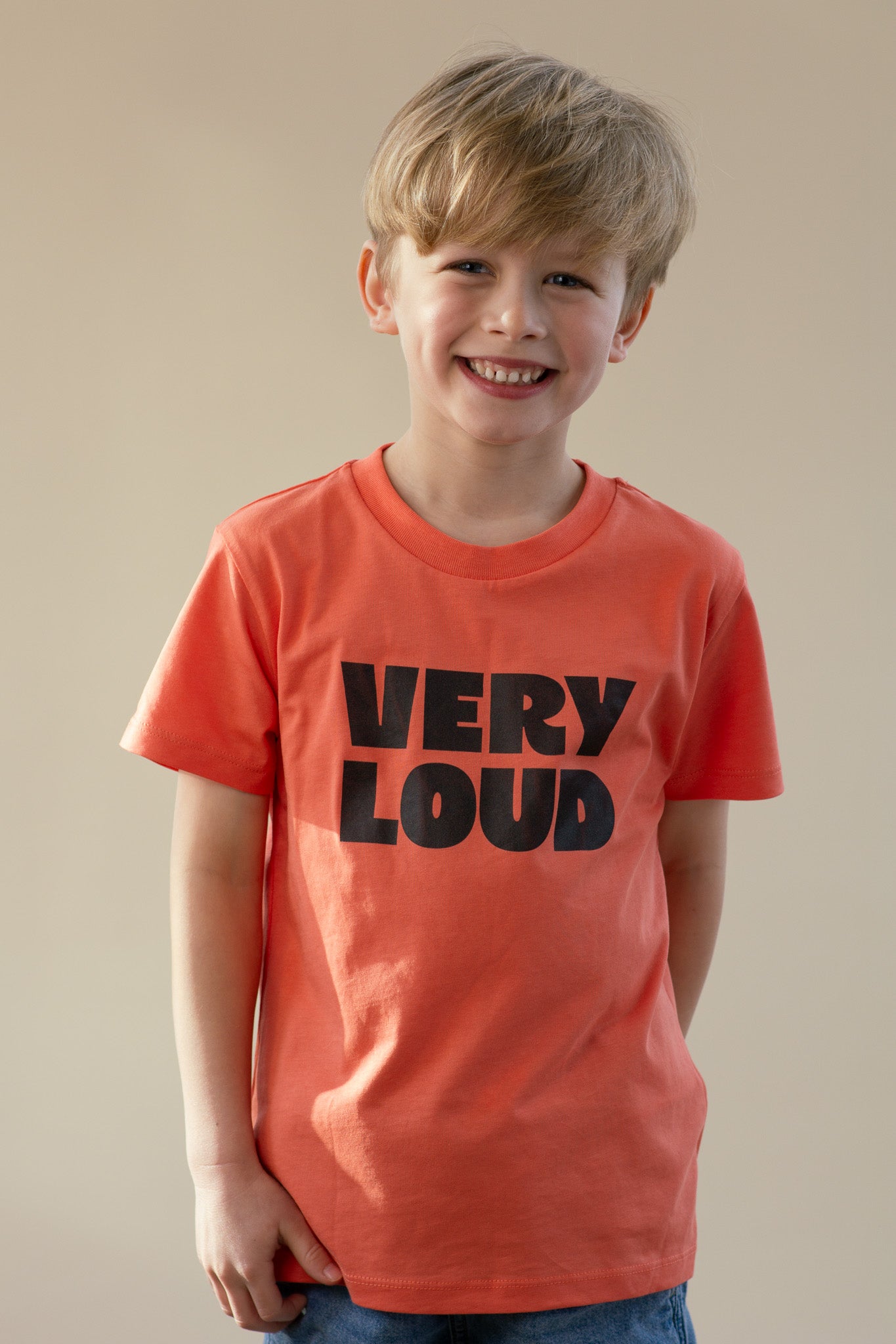 Child wearing an orange t-shirt with 'VERY LOUD' text on a plain background
