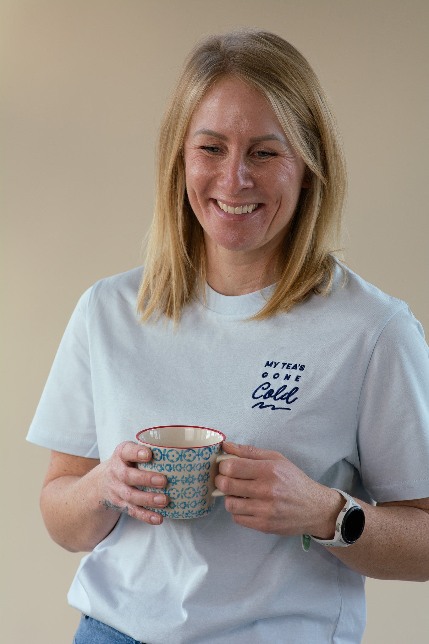 Woman holding a mug and wearing a blue t-shirt with 'My Tea's Gone Cold' text, against a plain background