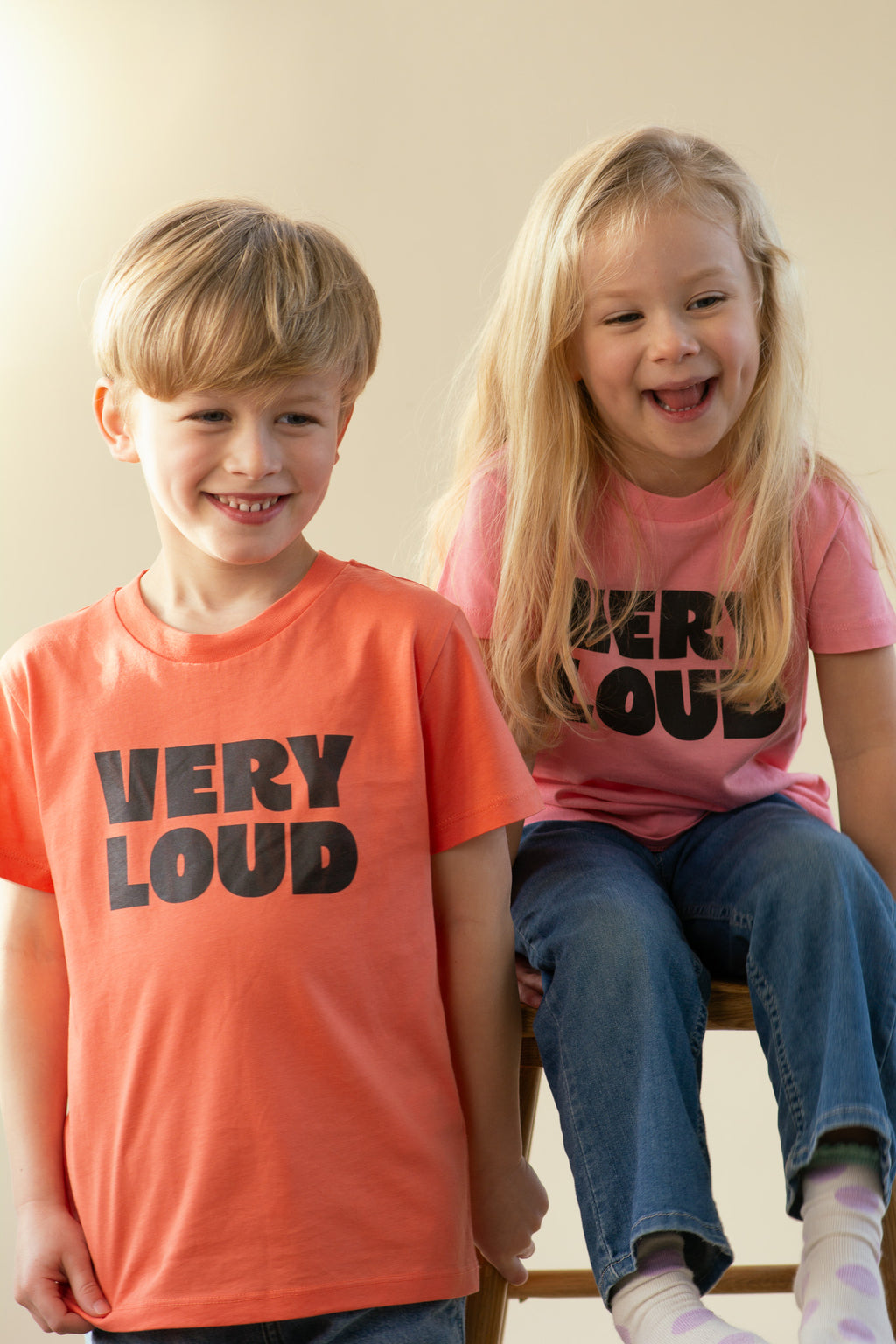 Two children wearing 'VERY LOUD' t-shirts sitting on a chair