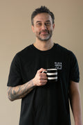 Man wearing a black t-shirt with 'Black Coffee Club' text, holding a striped mug against a beige background