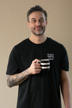 Man wearing a black t-shirt with 'Black Coffee Club' text, holding a striped mug against a beige background