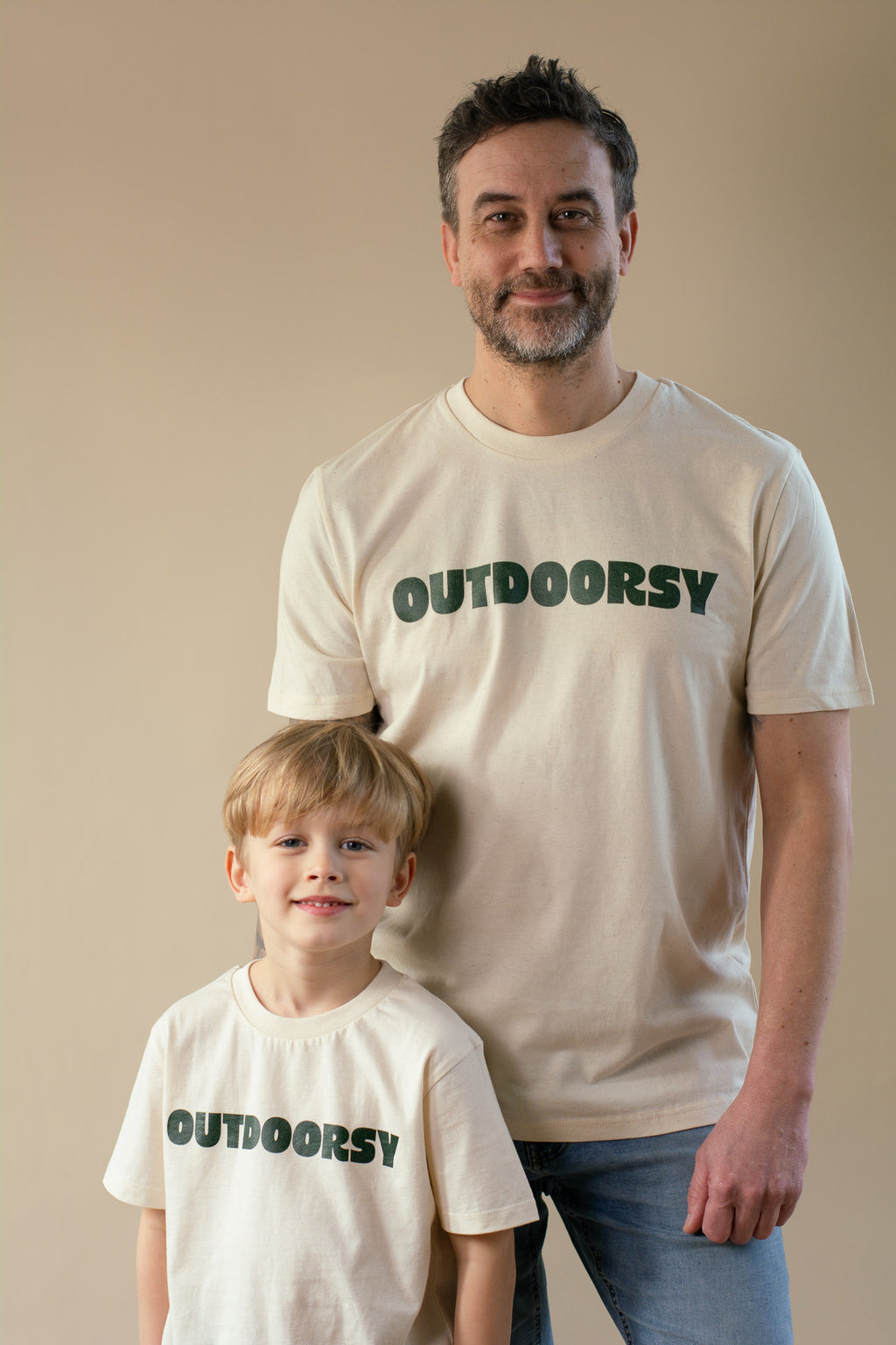 Man and child wearing 'OUTDOORSY' t-shirts against a beige background