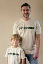 Man and child wearing 'OUTDOORSY' t-shirts against a beige background