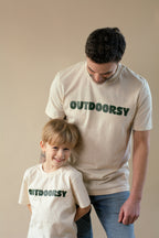 Man and child wearing 'OUTDOORSY' t-shirts against a beige background