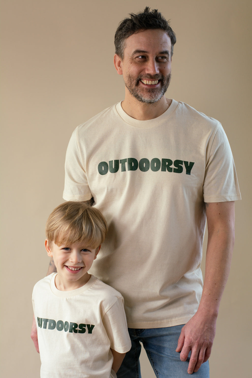 Man and child wearing 'OUTDOORSY' t-shirts against a beige background