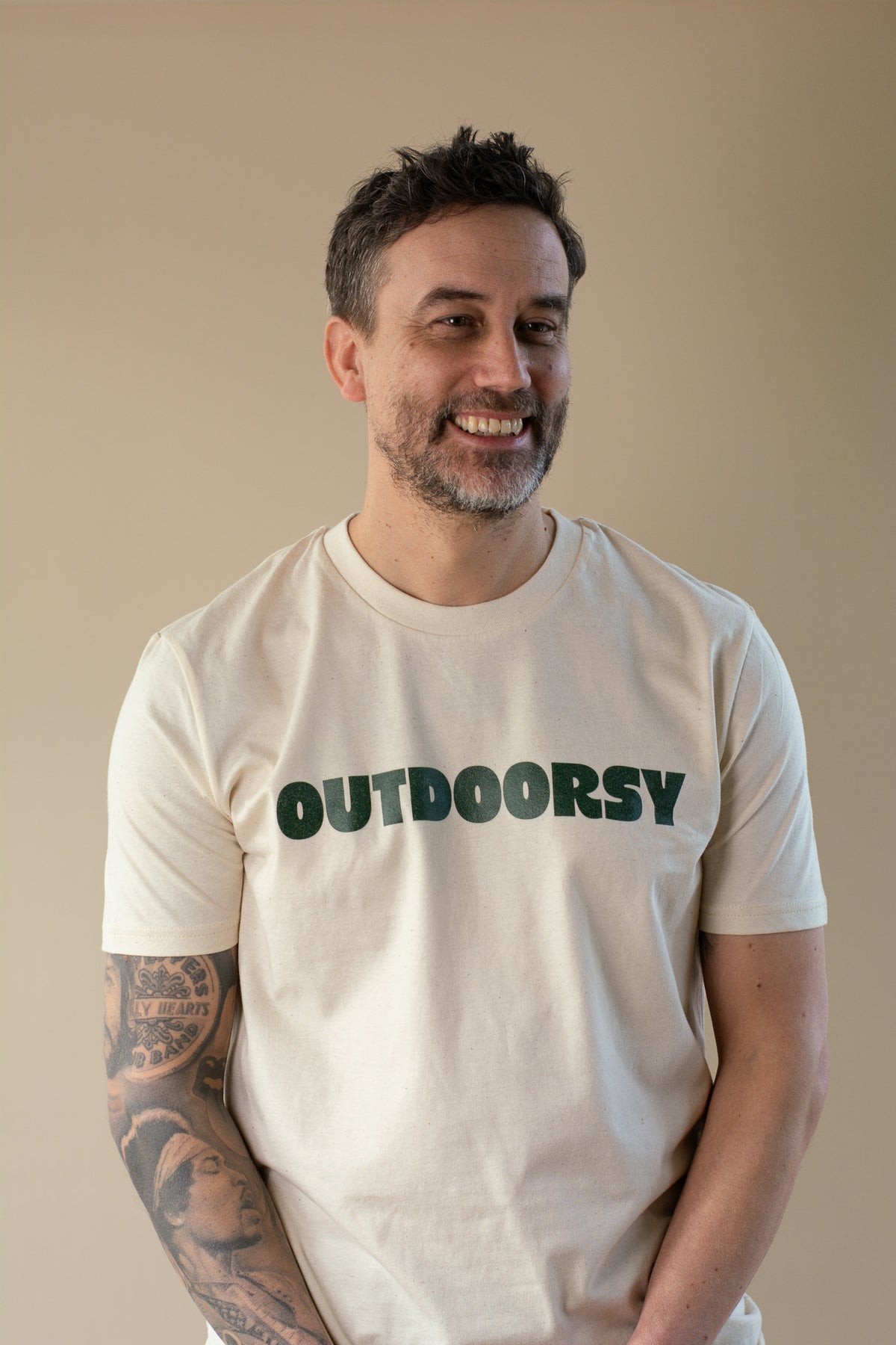 Man wearing a white t-shirt with 'OUTDOORSY' text on a beige background
