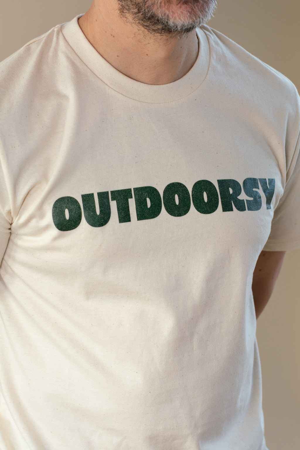 Person wearing a beige t-shirt with 'OUTDOORSY' printed in green text