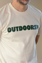 Person wearing a beige t-shirt with 'OUTDOORSY' printed in green text