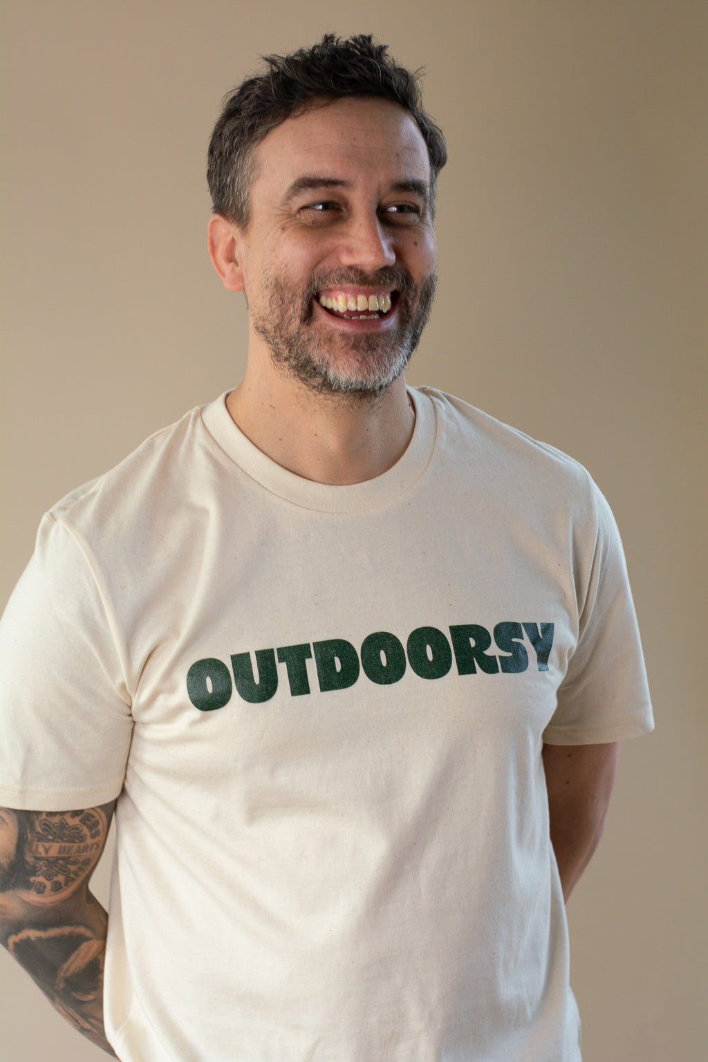 Man wearing a white t-shirt with 'OUTDOORSY' text, smiling against a plain background