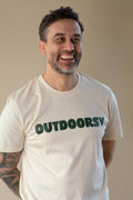 Man wearing a white t-shirt with 'OUTDOORSY' text, smiling against a plain background