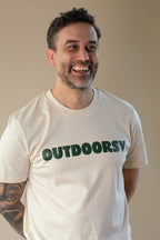 Man wearing a white t-shirt with 'OUTDOORSY' text, smiling against a plain background