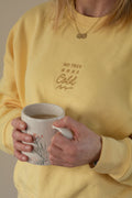 Person wearing a yellow sweatshirt with text holding a mug.