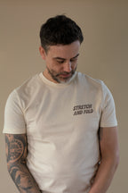 Man wearing a beige t-shirt with 'STRETCH AND FOLD' text, looking down.