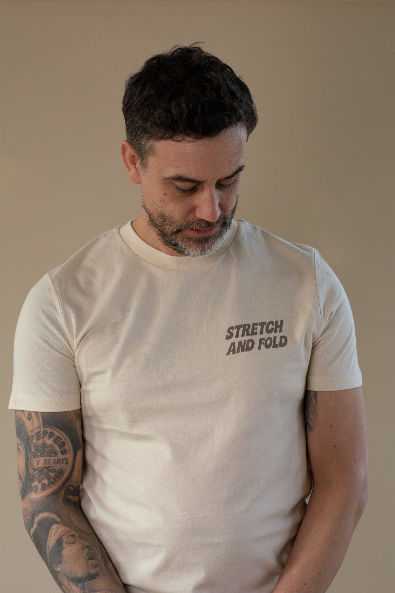 Man wearing a beige t-shirt with 'STRETCH AND FOLD' text, looking down.