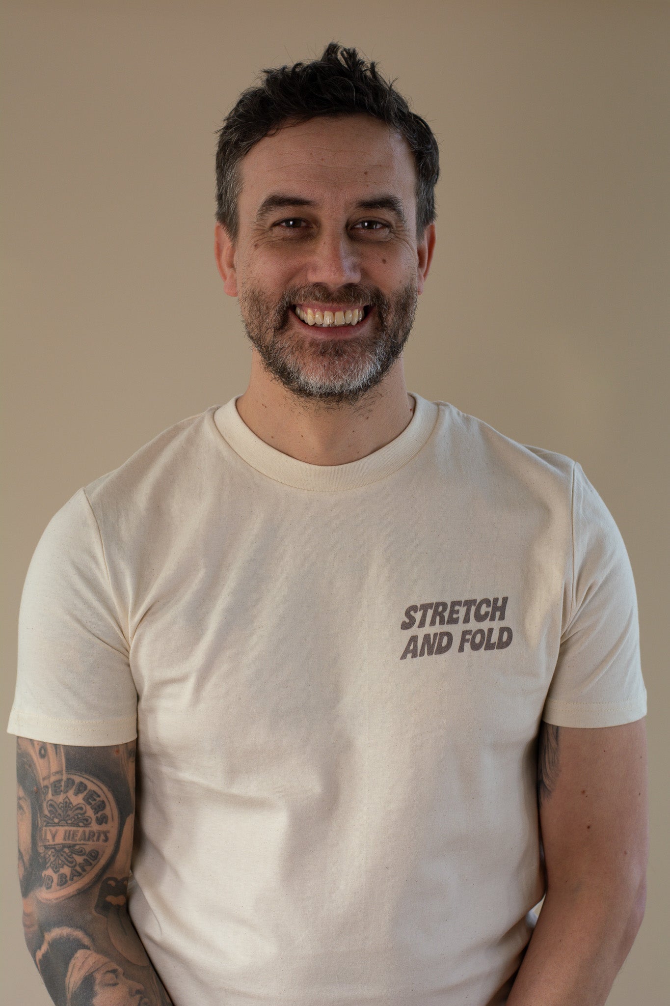 Man wearing a beige t-shirt with 'Stretch and Fold' text on a plain background