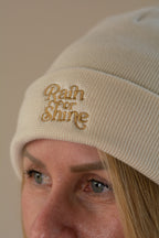 Beige beanie with 'Rain or Shine' embroidery worn by a person