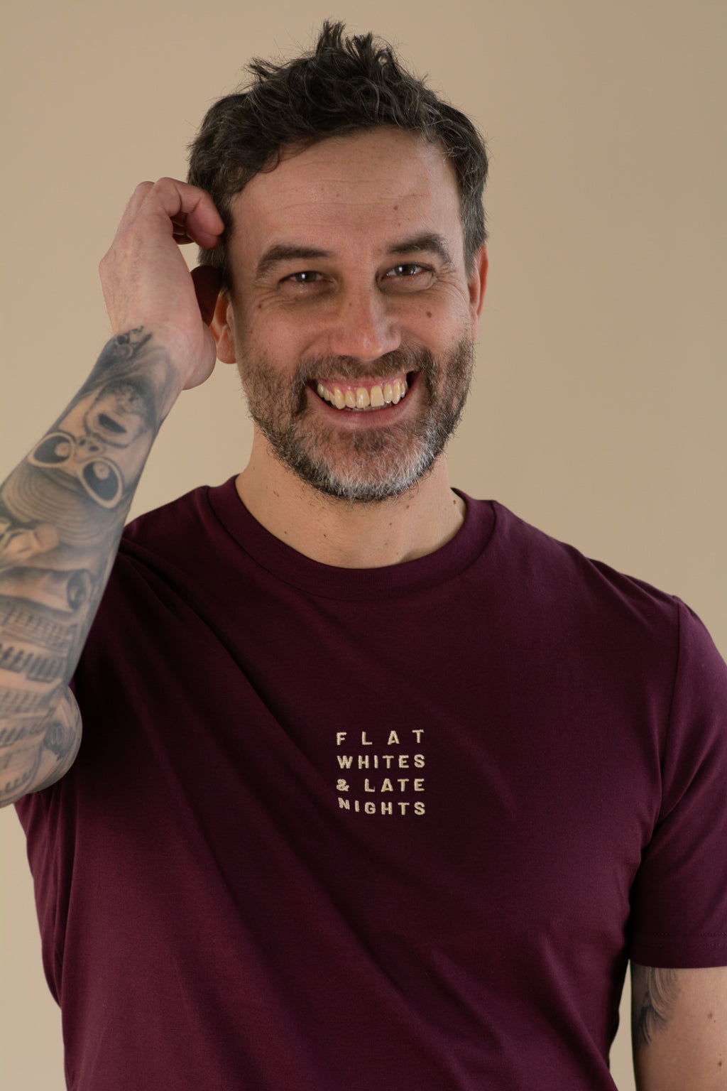 Man wearing a maroon t-shirt with text, smiling against a beige background