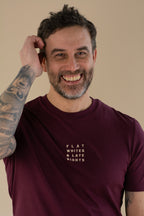 Man wearing a maroon t-shirt with text, smiling against a beige background