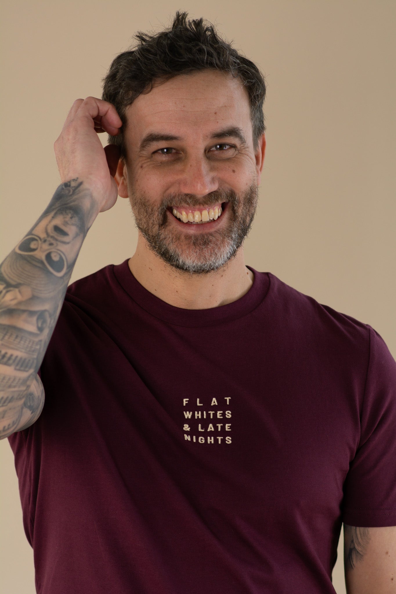 Man wearing a maroon t-shirt with text, smiling against a beige background