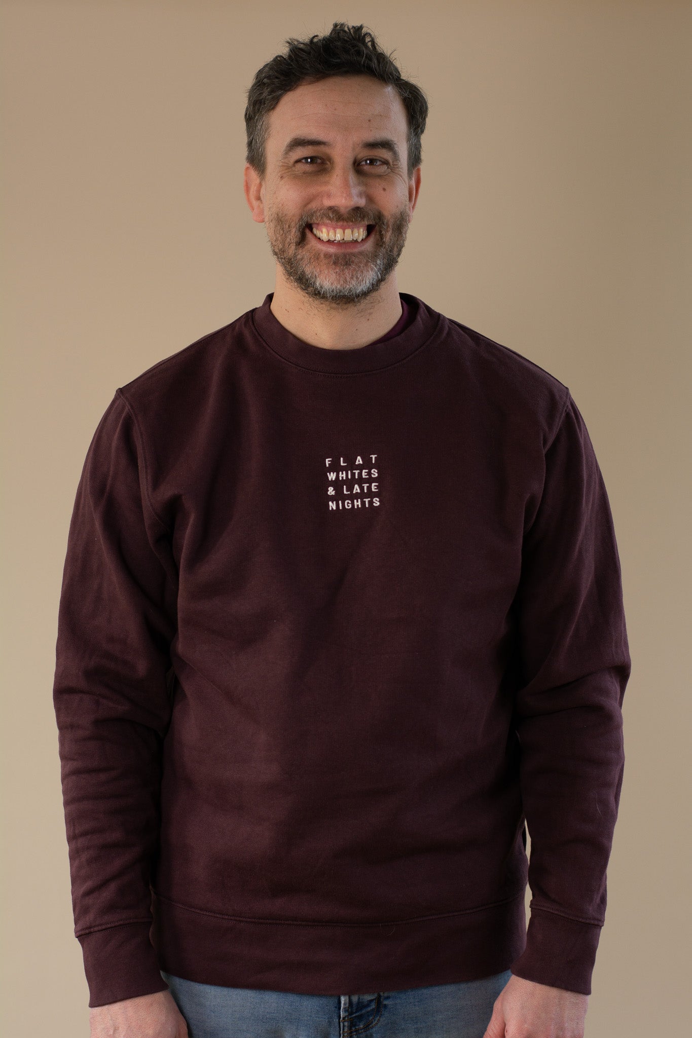 Man wearing a maroon sweatshirt with 'FLAT WHITES & LATE NIGHTS' text on a beige background