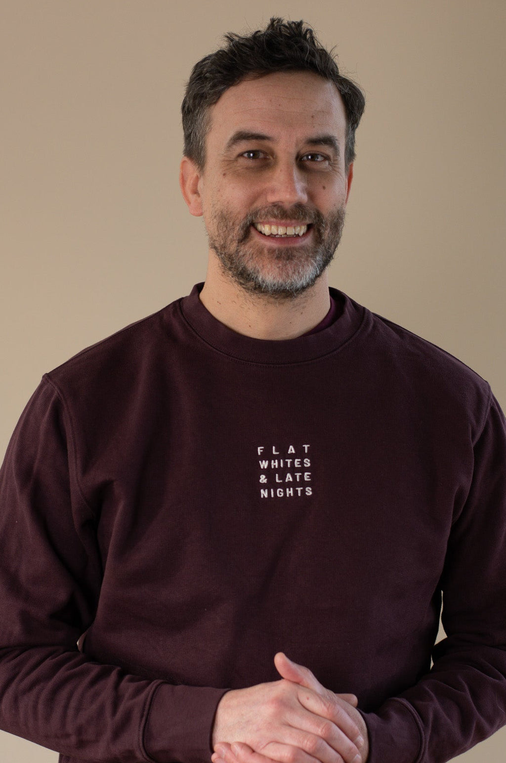 Man wearing a maroon sweatshirt with 'FLAT WHITES & LATE NIGHTS' text on a beige background