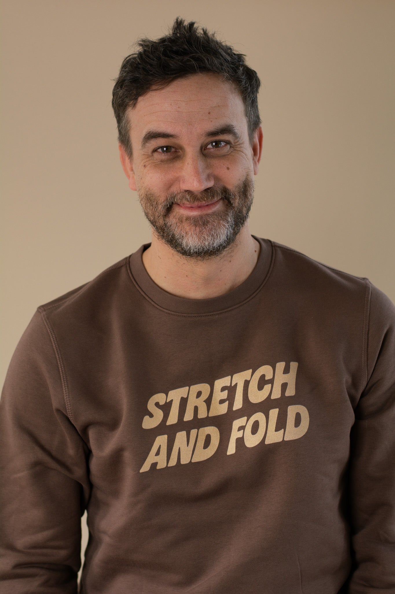 Man wearing a brown sweatshirt with 'STRETCH AND FOLD' text against a beige background