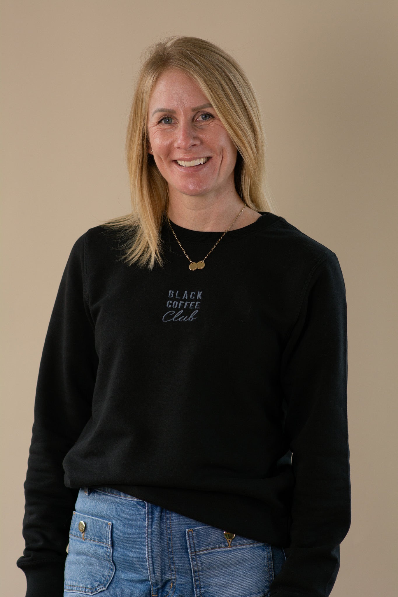 Woman wearing a black sweatshirt with 'Black Coffee Club' text on a beige background