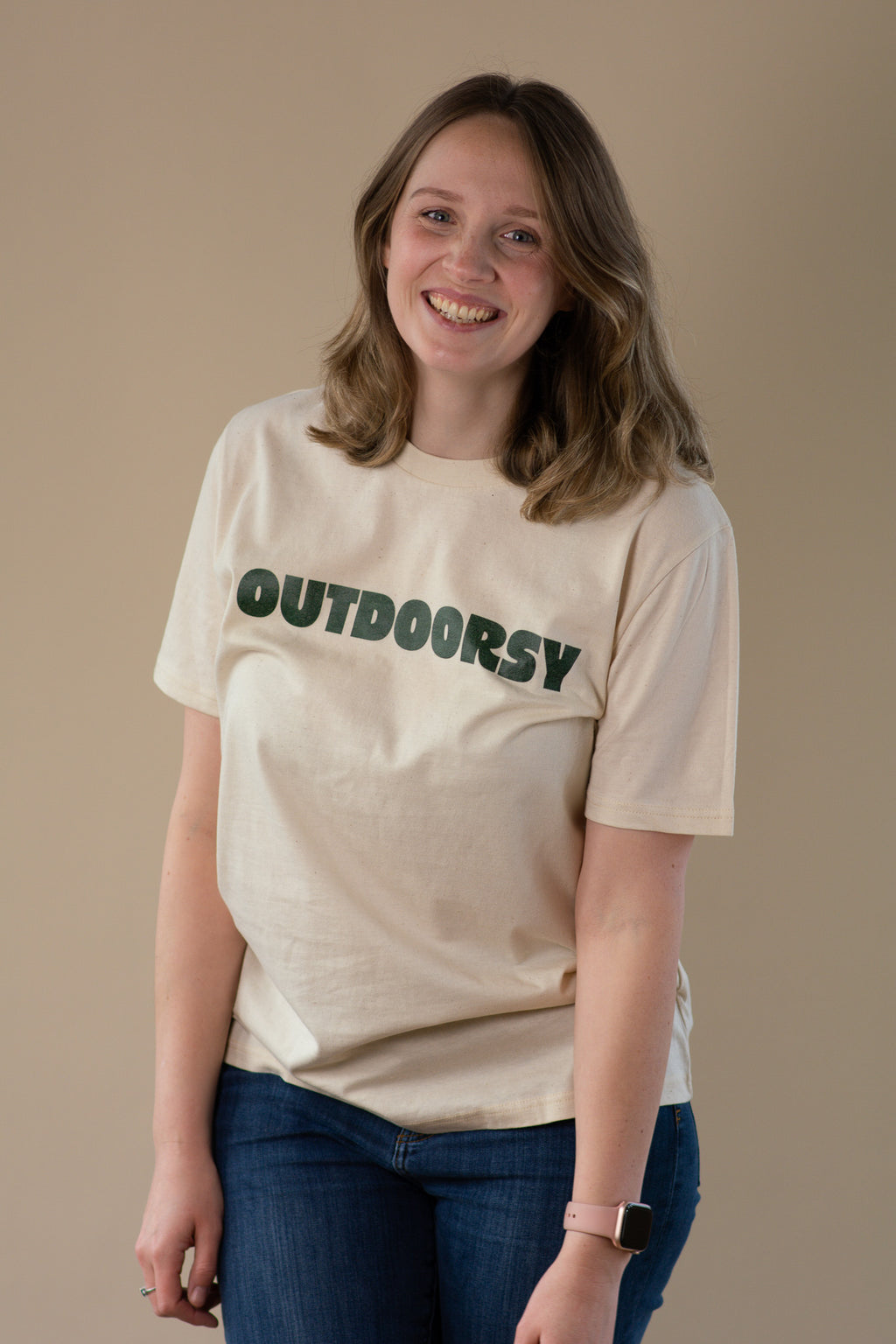 Person wearing a beige t-shirt with 'OUTDOORSY' text on a plain background