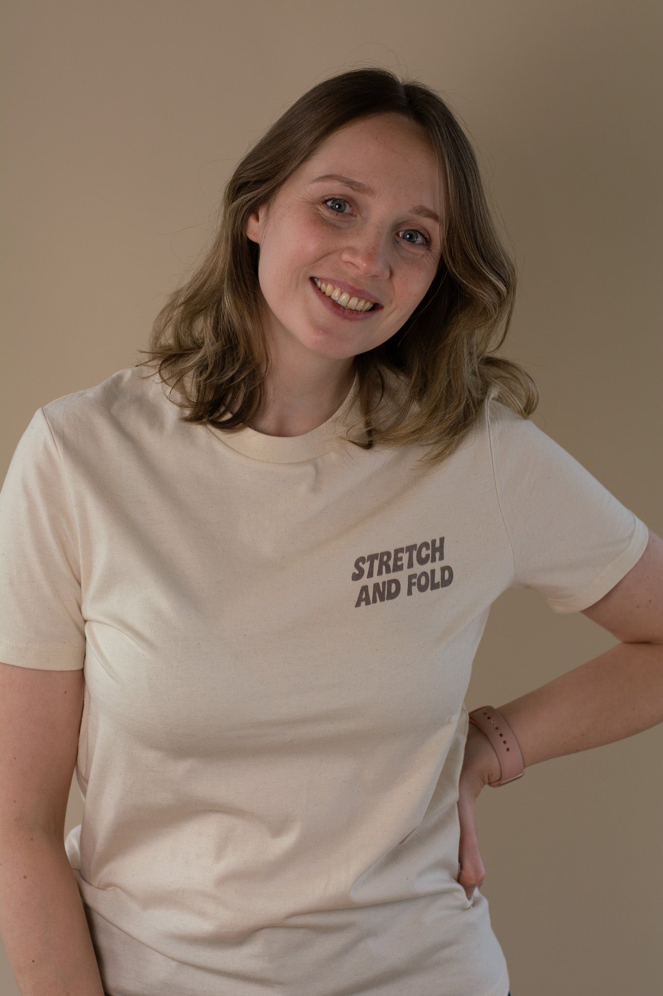Person wearing a beige t-shirt with 'Stretch and Fold' text on a plain background