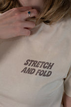 Beige t-shirt with 'STRETCH AND FOLD' text worn by a person.