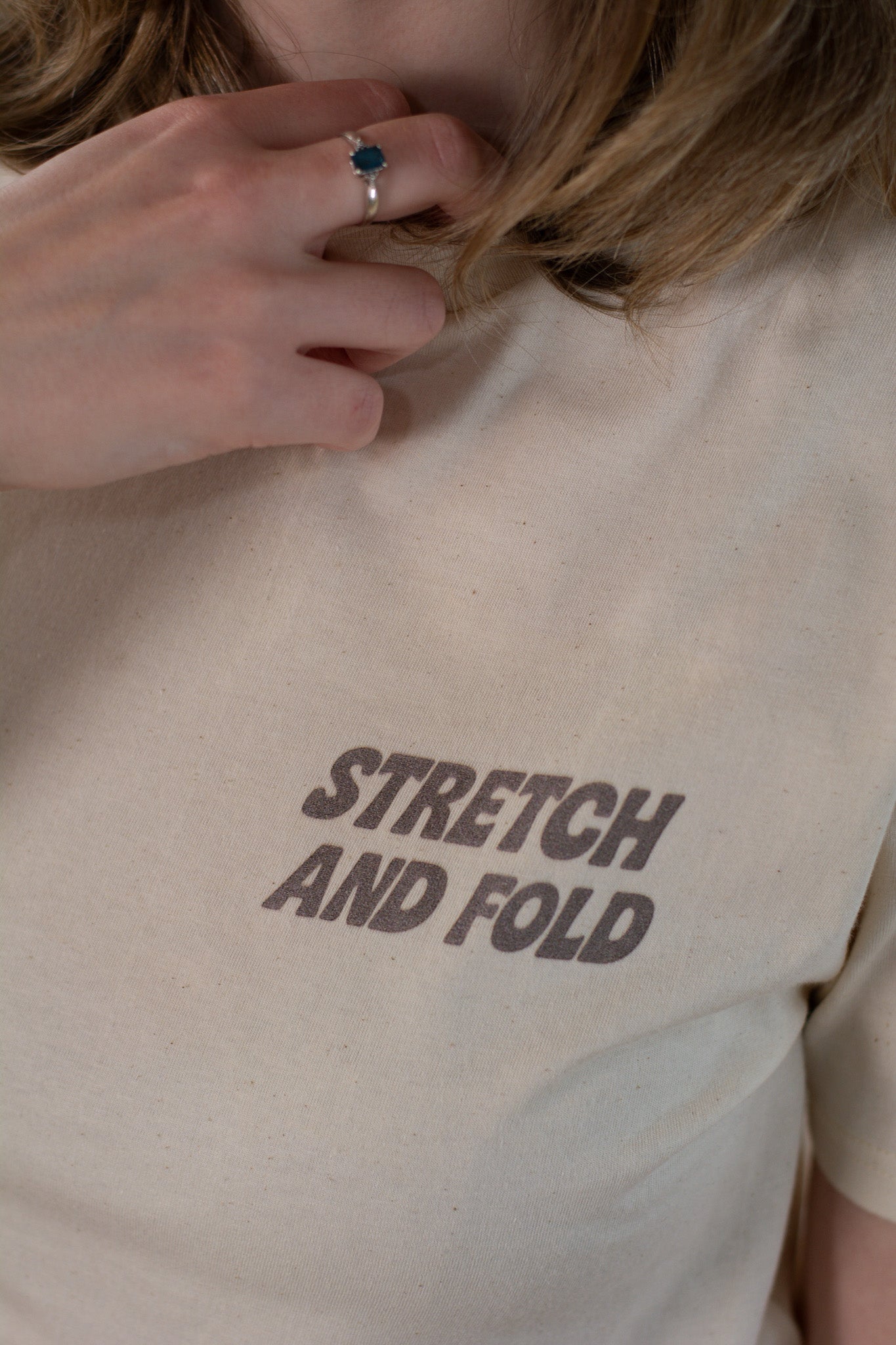 Beige t-shirt with 'STRETCH AND FOLD' text worn by a person.