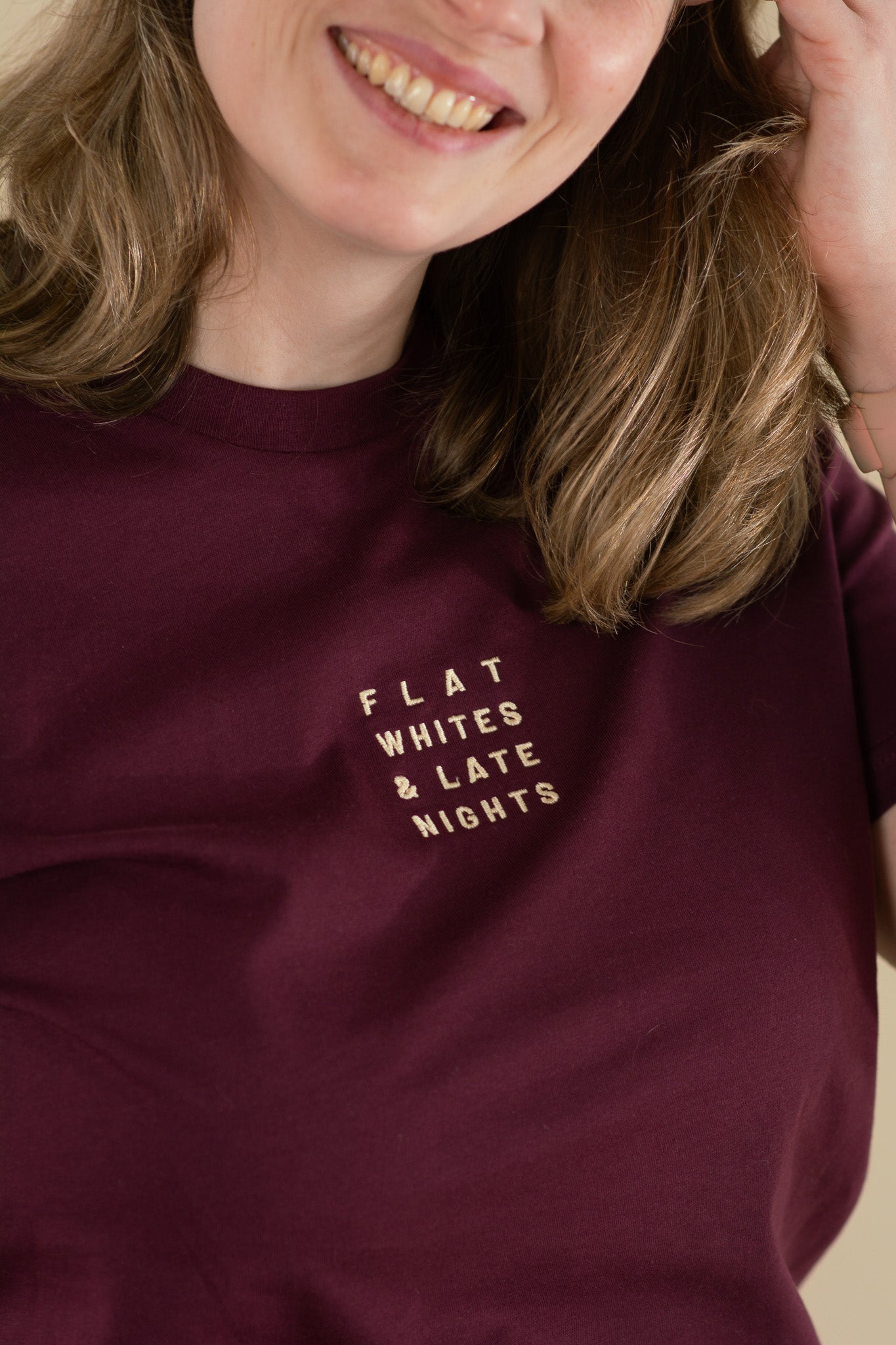 Person wearing a maroon sweatshirt with 'FLAT WHITES & LATE NIGHTS' text
