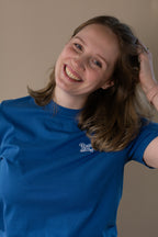 Person wearing a blue t-shirt with a logo, posing against a plain background