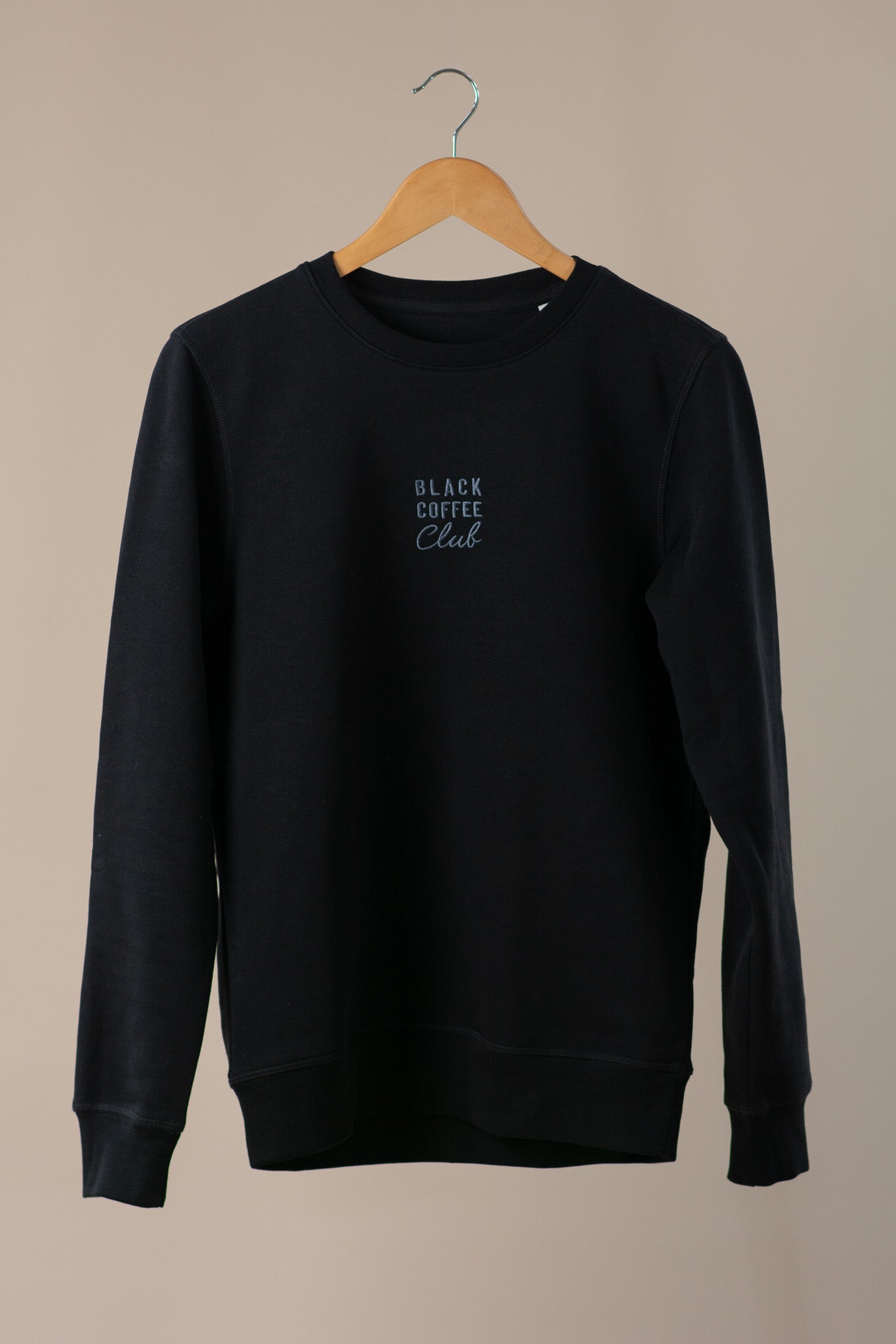 Black sweatshirt with 'Black Coffee Club' text on a beige background