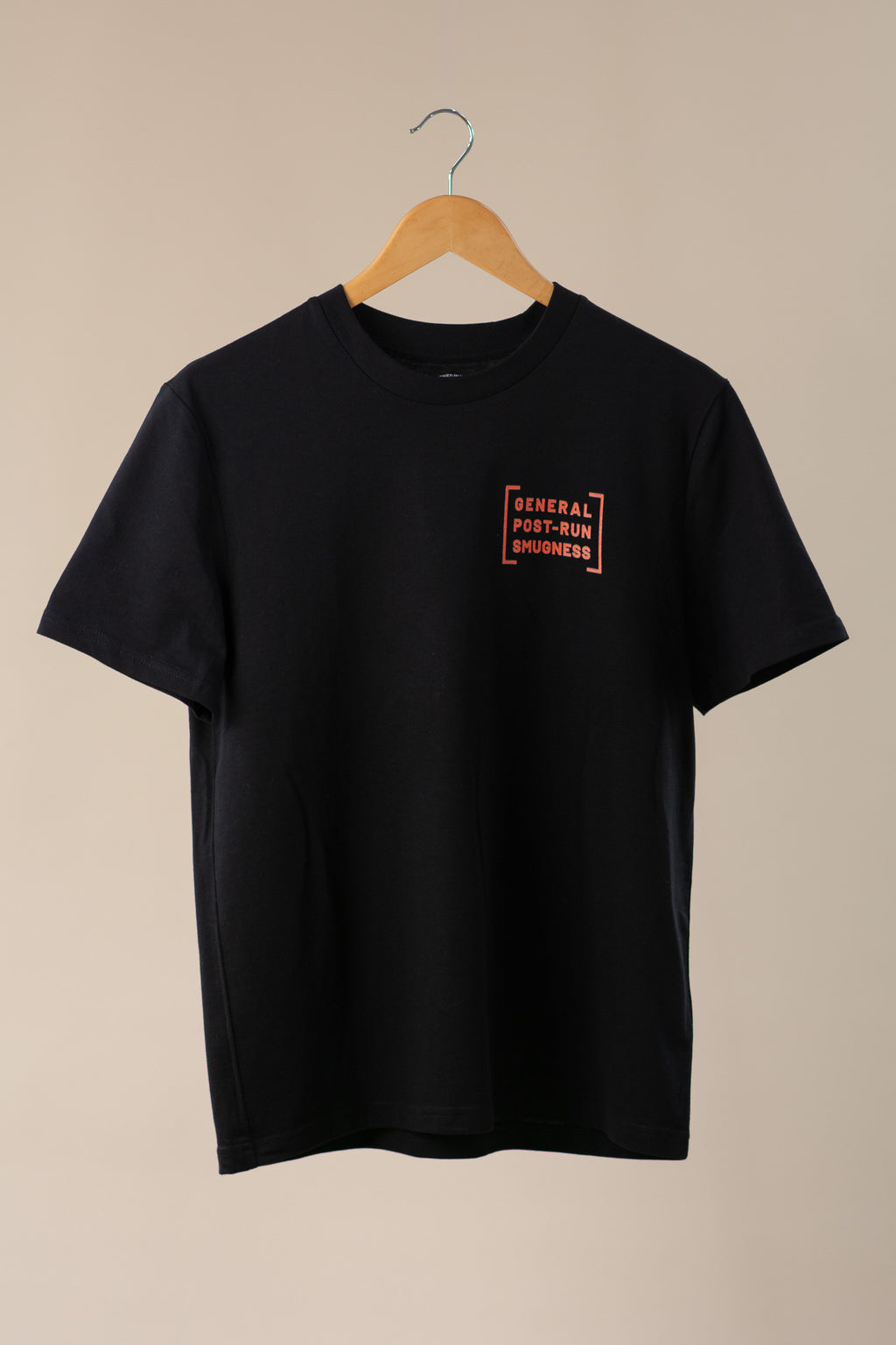 Black t-shirt with orange logo on a wooden hanger against a beige background
