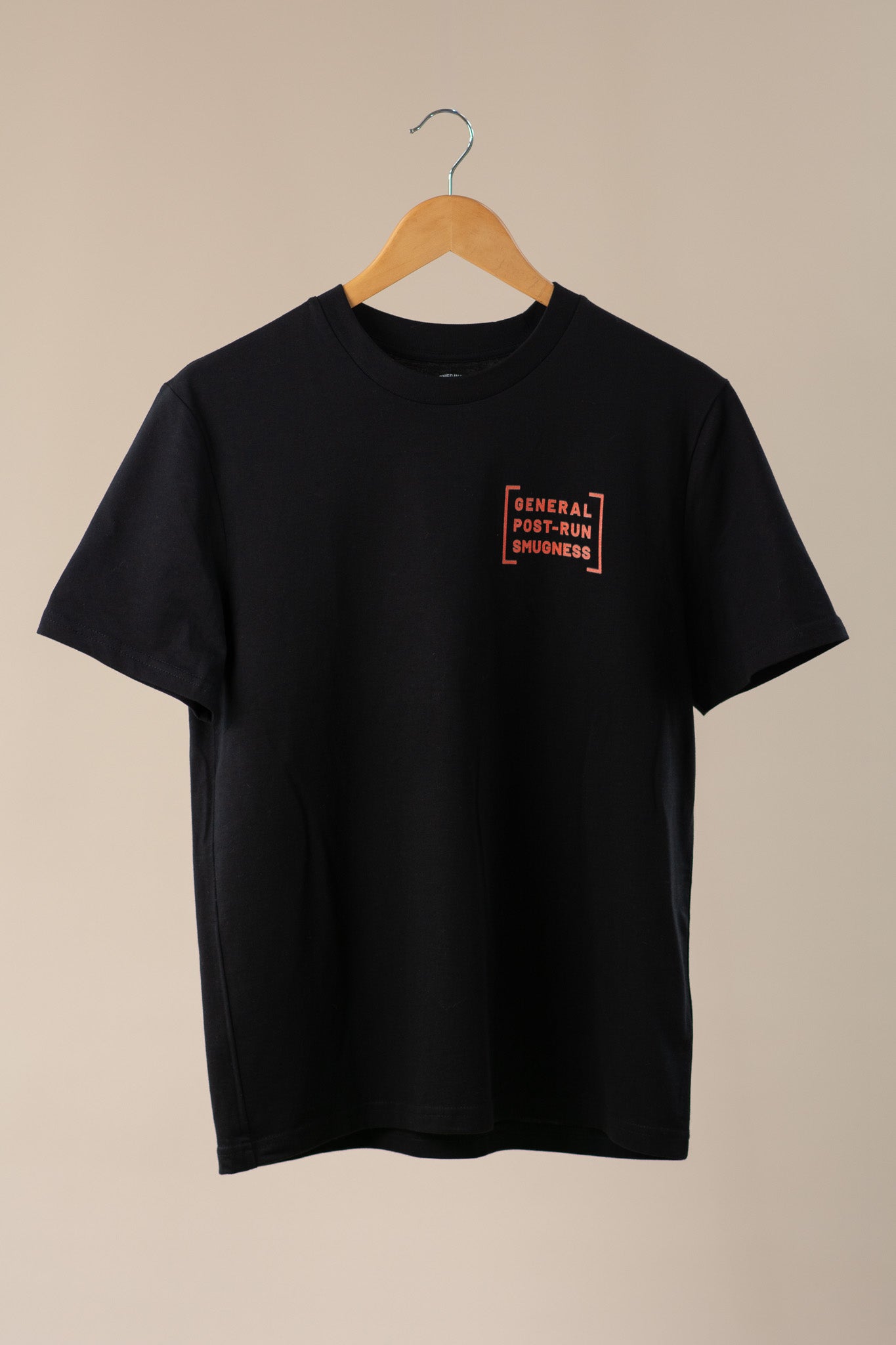Black t-shirt with orange logo on a wooden hanger against a beige background