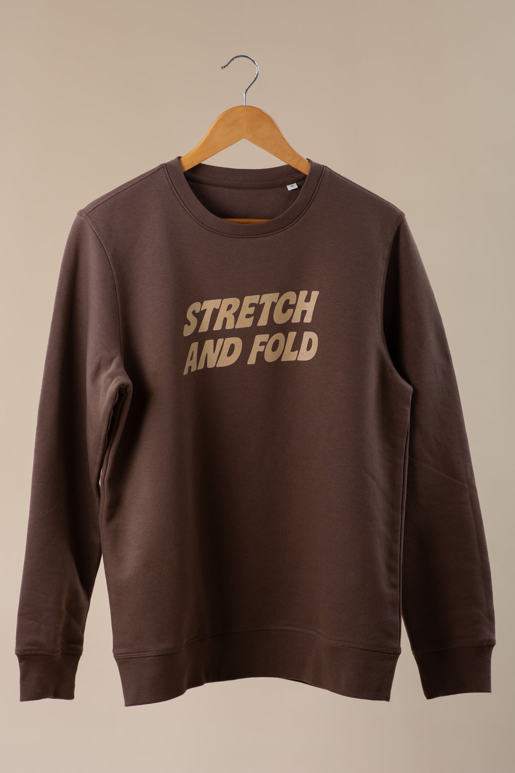 Brown sweatshirt with 'STRETCH AND FOLD' text on a beige background