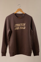 Brown sweatshirt with 'STRETCH AND FOLD' text on a beige background