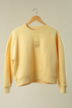 Yellow sweatshirt on a wooden hanger against a beige background