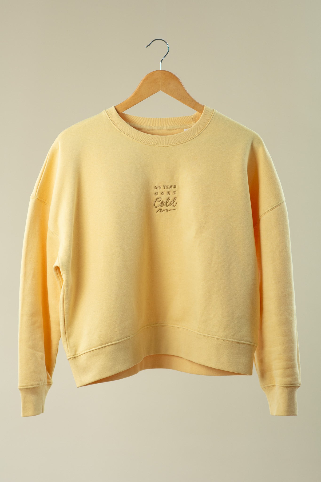 Yellow sweatshirt on a wooden hanger against a beige background