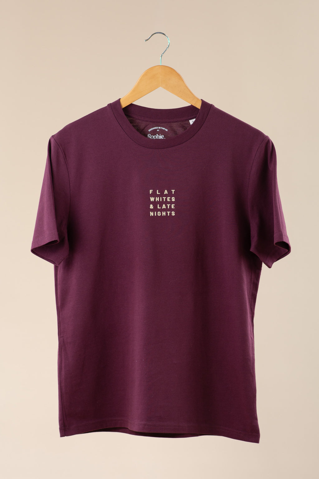 Maroon t-shirt with text on a hanger against a beige background