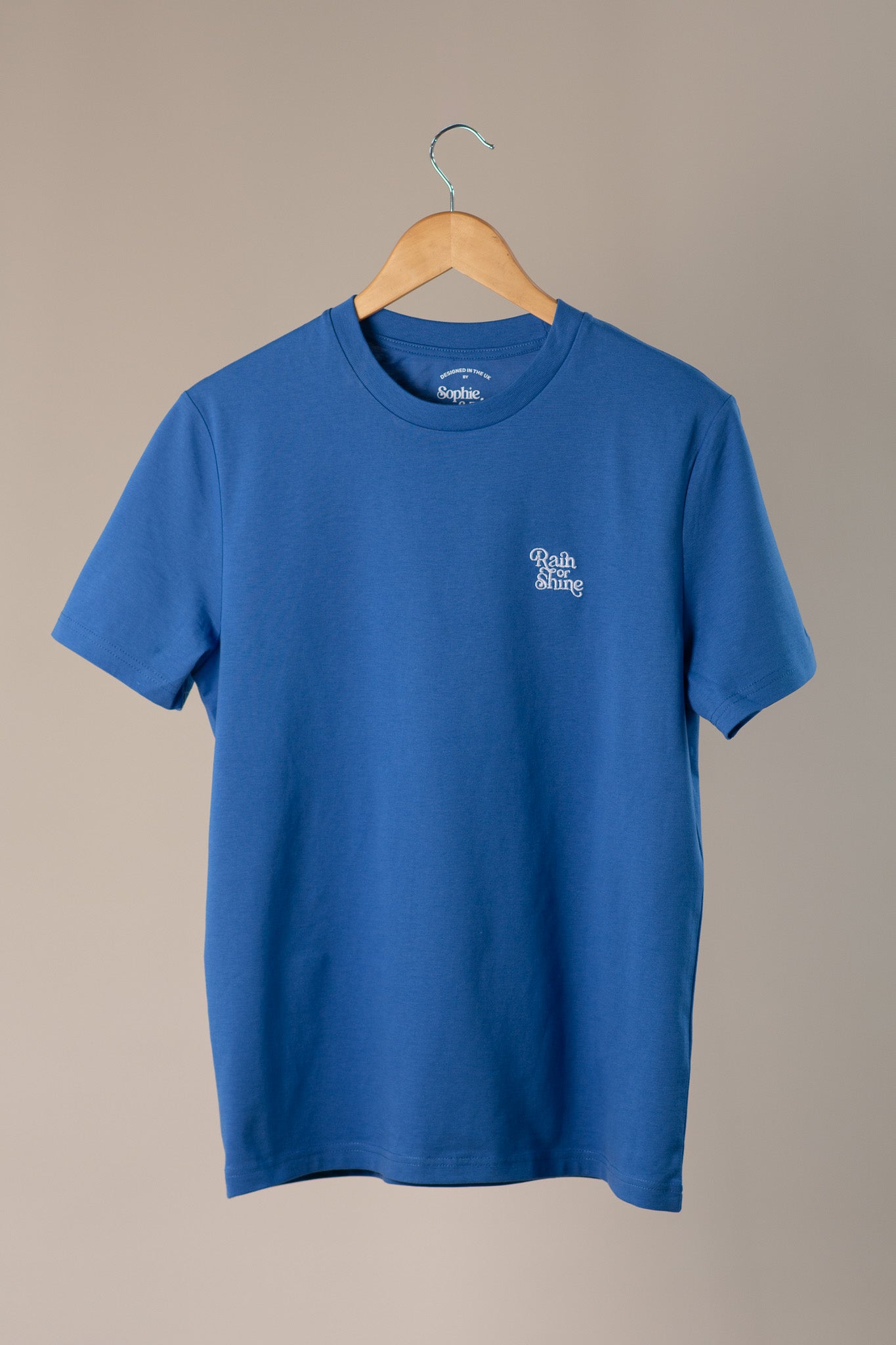 Blue t-shirt with a logo on a wooden hanger against a beige background