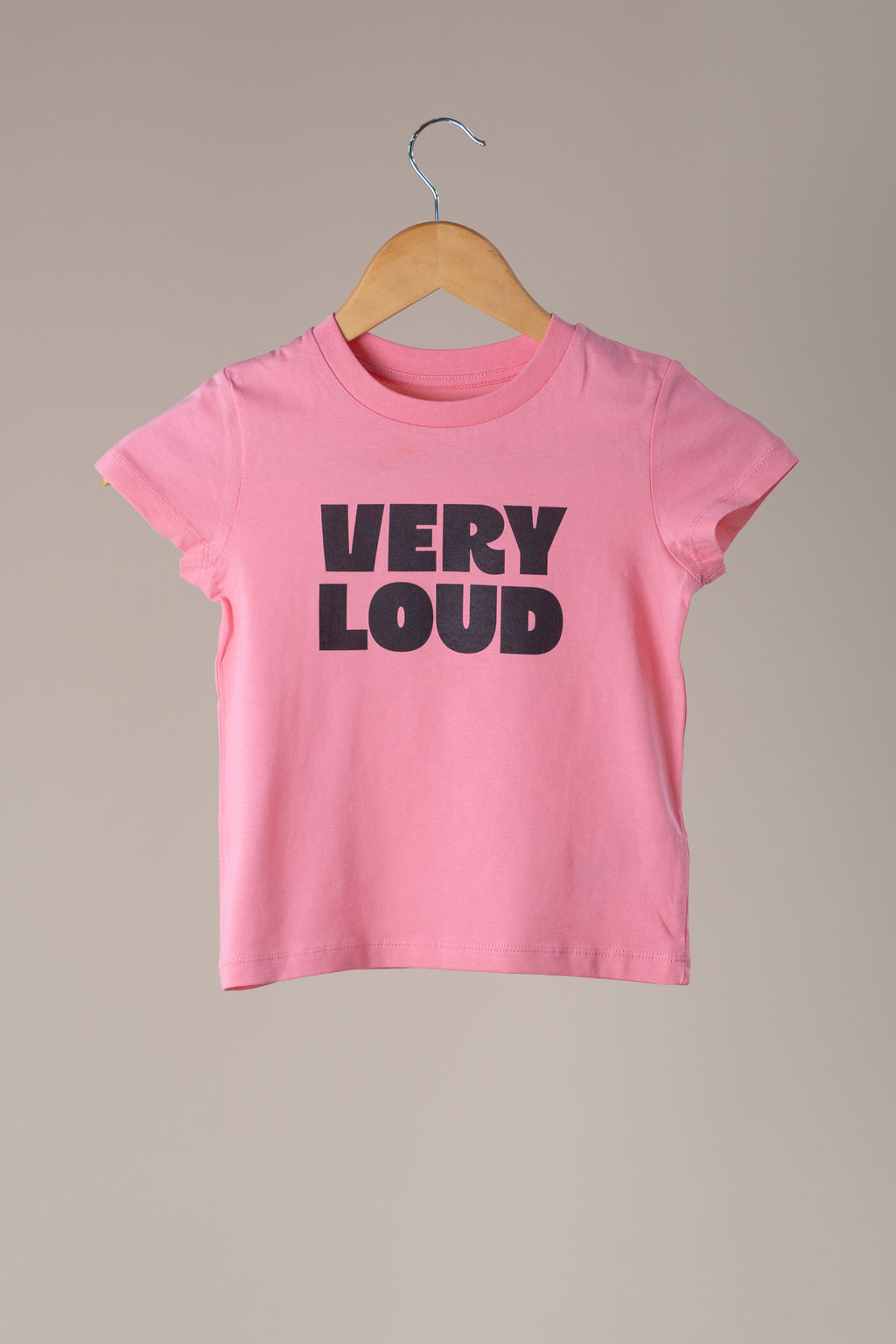 Pink t-shirt with 'VERY LOUD' text on a hanger against a beige background
