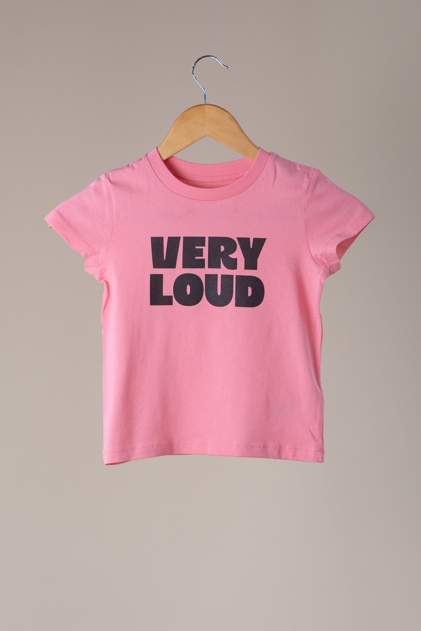 Pink t-shirt with 'VERY LOUD' text on a hanger against a beige background