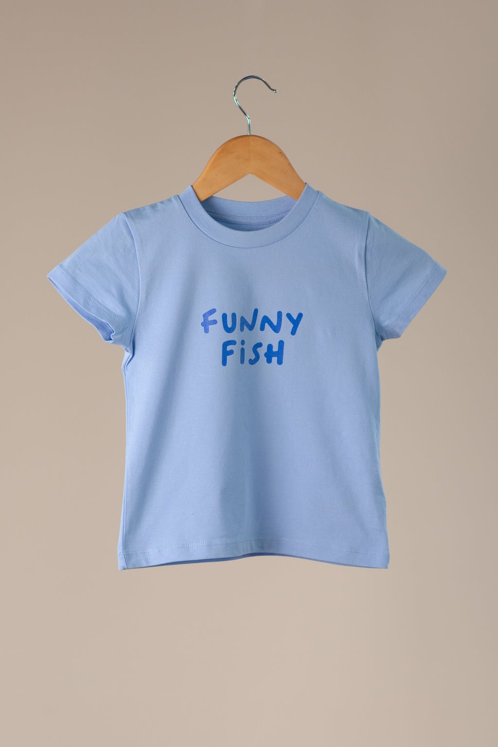 Light blue t-shirt with 'FUNNY FISH' text on a wooden hanger against a beige background